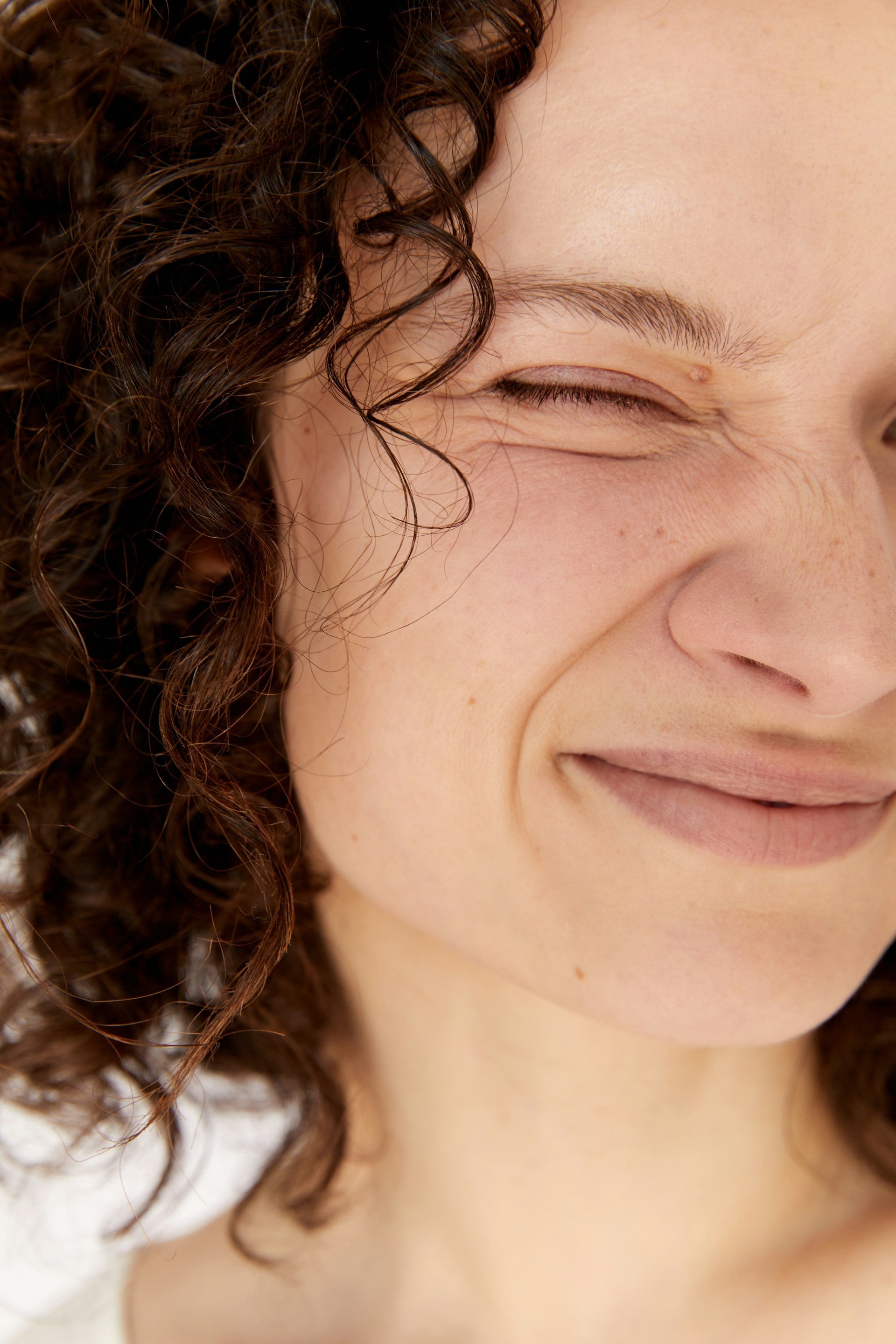 Close up of woman with curly hair smiling at camera and crinkling her nose