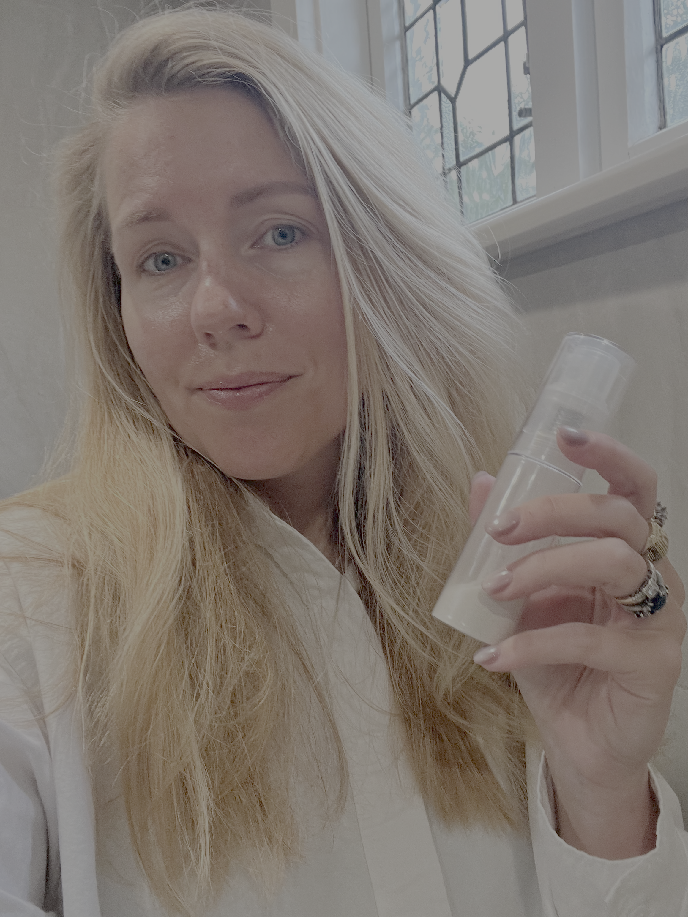 Woman holding a bottle of No Scrubs dry shampoo indoors with a window in the background